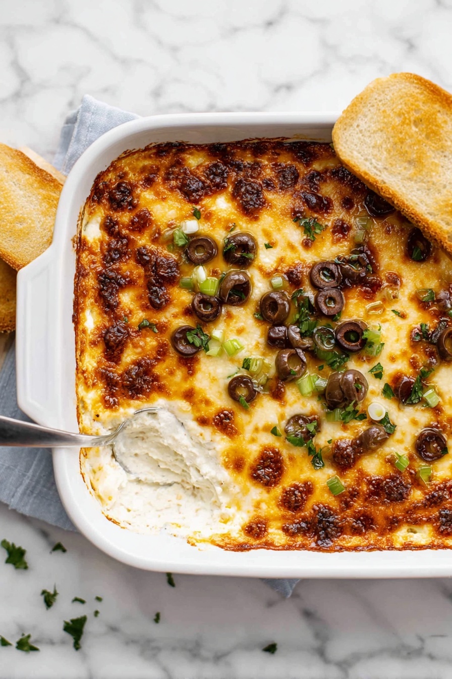 Cheesy Olive Baked Dip, cheesy olive dip, savory baked dip, cheesy appetizer, easy party dip - A rectangular white baking dish filled with a layered casserole. The top layer is golden brown melted cheese with some darker brown crisp spots scattered unevenly. Beneath the cheese, hints of creamy sauce can be seen bubbling at the edges. The dish sits on a white marbled surface with a black and white striped cloth on the left side. The texture of the melted cheese appears smooth with bubbly areas, covering the whole top evenly. photo taken with an iphone --ar 2:3 --v 7